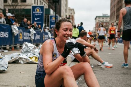 Marathonienne épuisée assise sur un trottoir après la course, buvant une boisson électrolytique de récupération